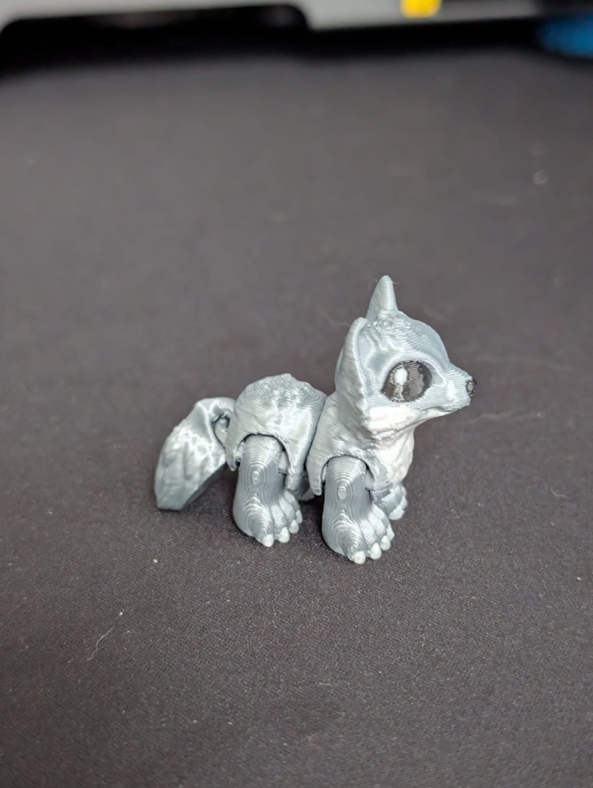 A small silver-gray articulated animal figurine, resembling a fox or chipmunk, sitting on a dark gray surface.