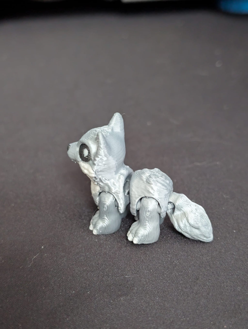 A small unpainted gray 3D-printed articulated animal figure resembling a fox or wolf cub, shown on a dark gray surface.
