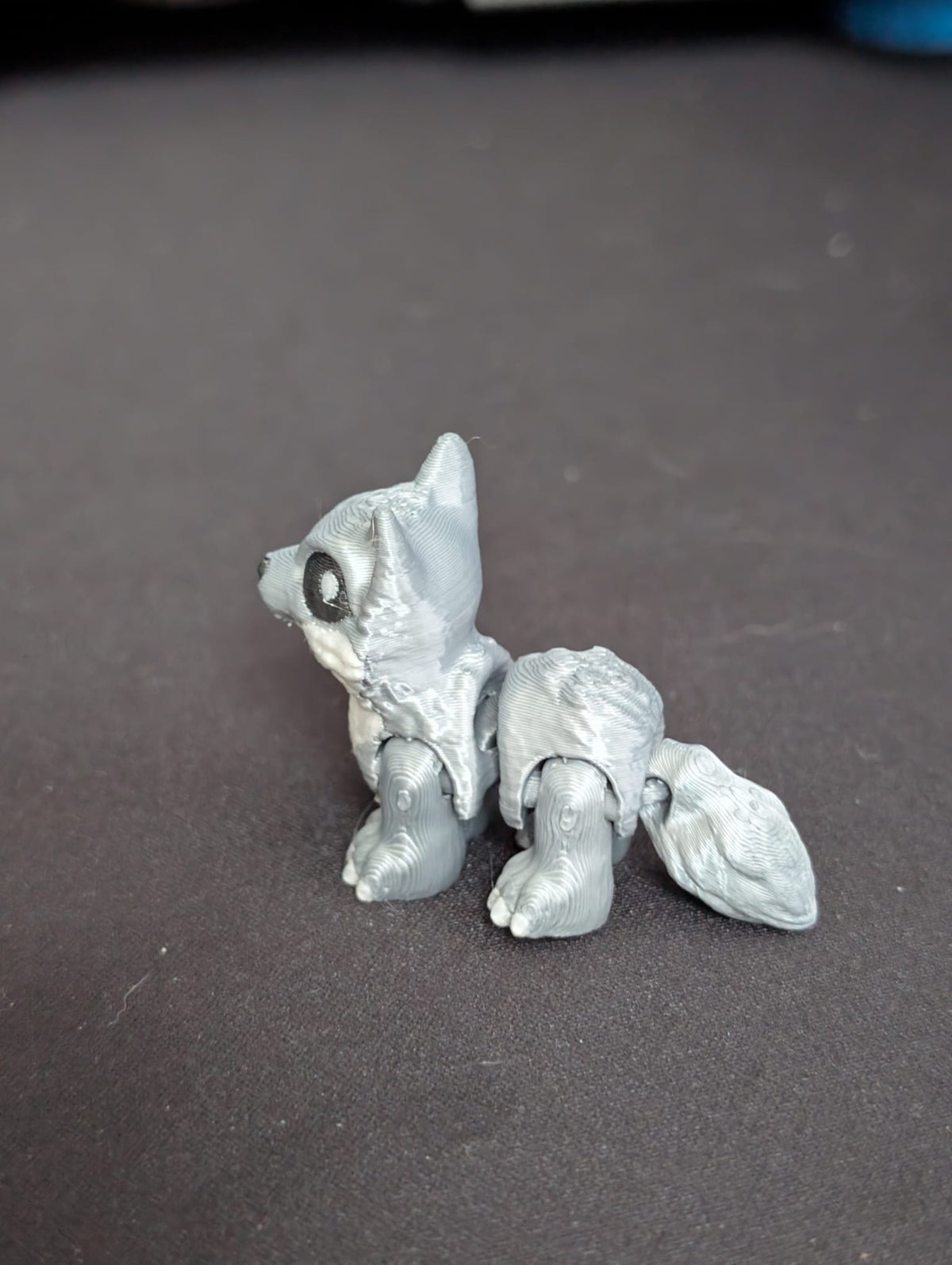 A small unpainted gray 3D-printed articulated animal figure resembling a fox or wolf cub, shown on a dark gray surface.
