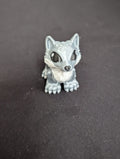 A small gray and white wolf figurine with large black eyes, standing on a dark gray surface.