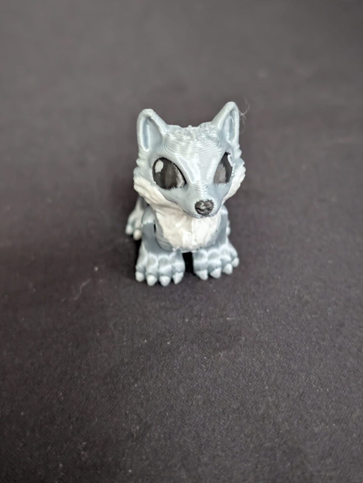 A small gray and white wolf figurine with large black eyes, standing on a dark gray surface.